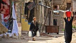 فلسطينيتان تحملان جالونات من المياه في مخيم درعا 