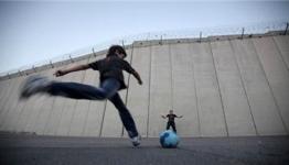 طفل فلسطيني يسدد الكرة على جدار الفصل العنصري 