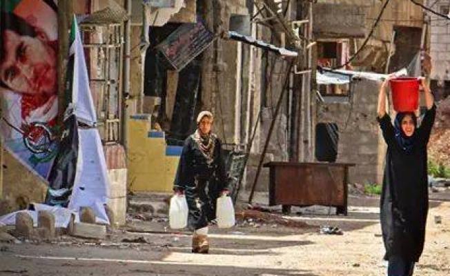 فلسطينيتان تحملان جالونات من المياه في مخيم درعا